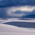 Dune Rain – fine art photograph of a rain shaft falling over mountains beyond the white dunes of White Sands National Park, New Mexico, by Aaron Chang
