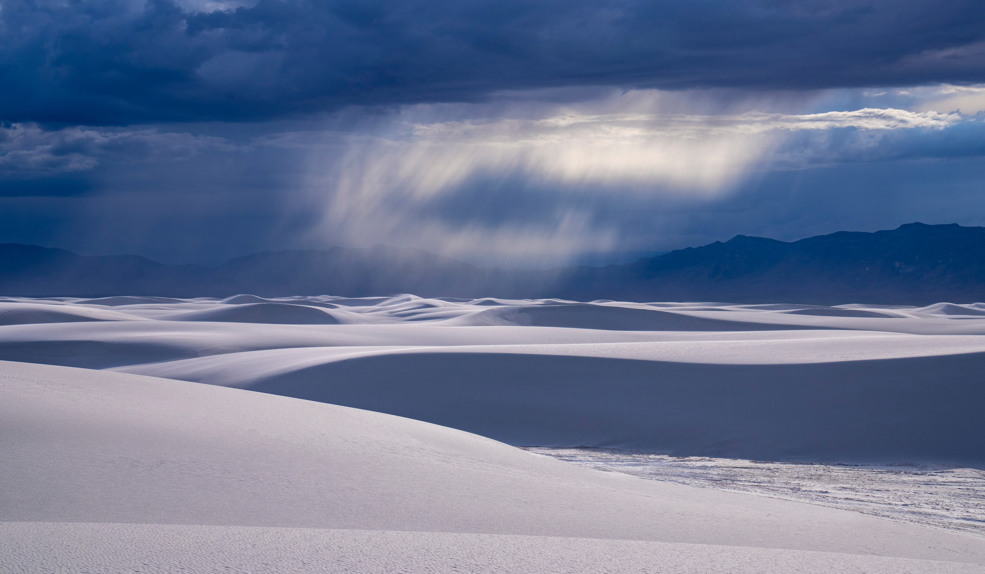 Dune Rain – fine art photograph of a rain shaft falling over mountains beyond the white dunes of White Sands National Park, New Mexico, by Aaron Chang